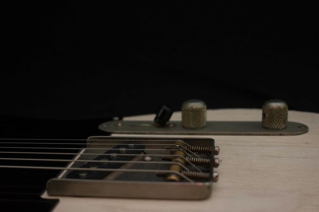 Moody studio macro of a blonde Telecaster-style bridge plate and control knobs against a black background.