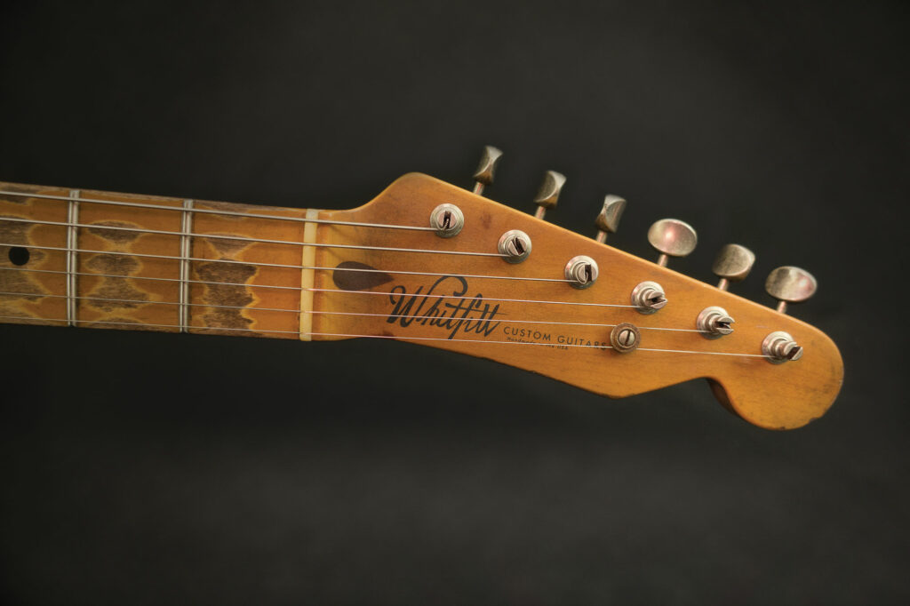 Gibson Les Paul headstock resting on a glass table in a warm interior, gold logo and crown inlay catching the light.