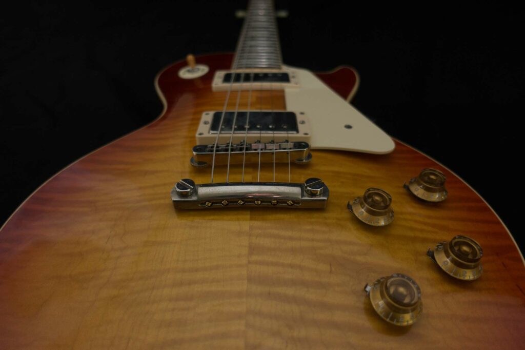 Macro detail of a cherry-sunburst Les Paul's flame-maple top, humbuckers, and bridge against black.