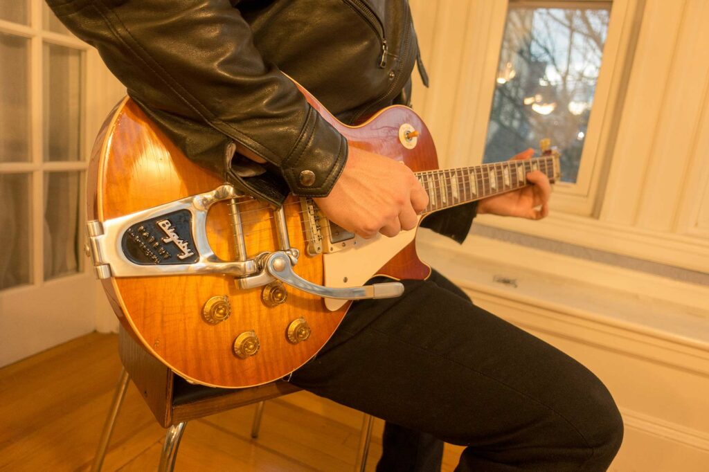Player cradling a sunburst Les Paul with a Bigsby vibrato, the flame-maple top glowing in golden afternoon light.