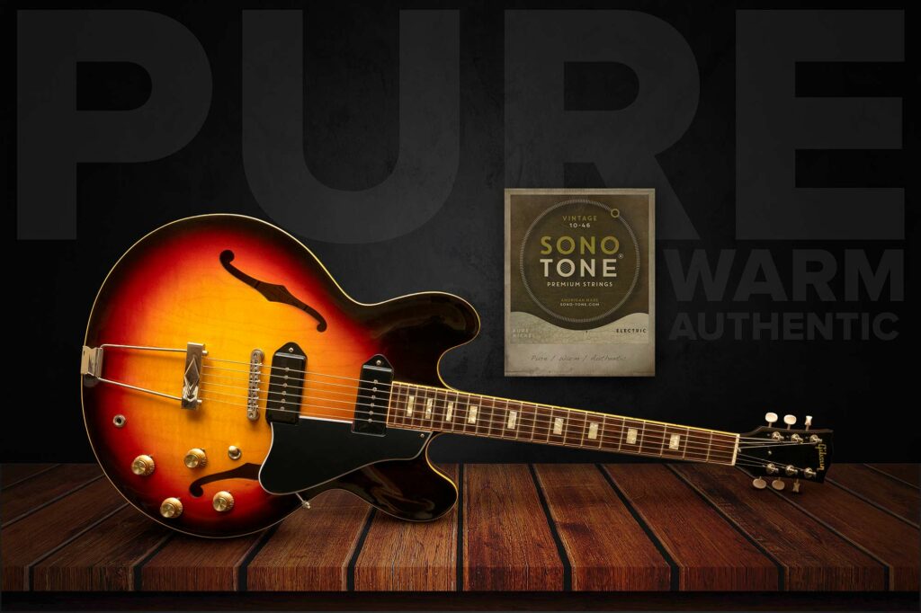 Sunburst Gibson hollowbody beside a SonoTone Vintage string pack with Pure / Warm / Authentic lettering on a dark plank wall.