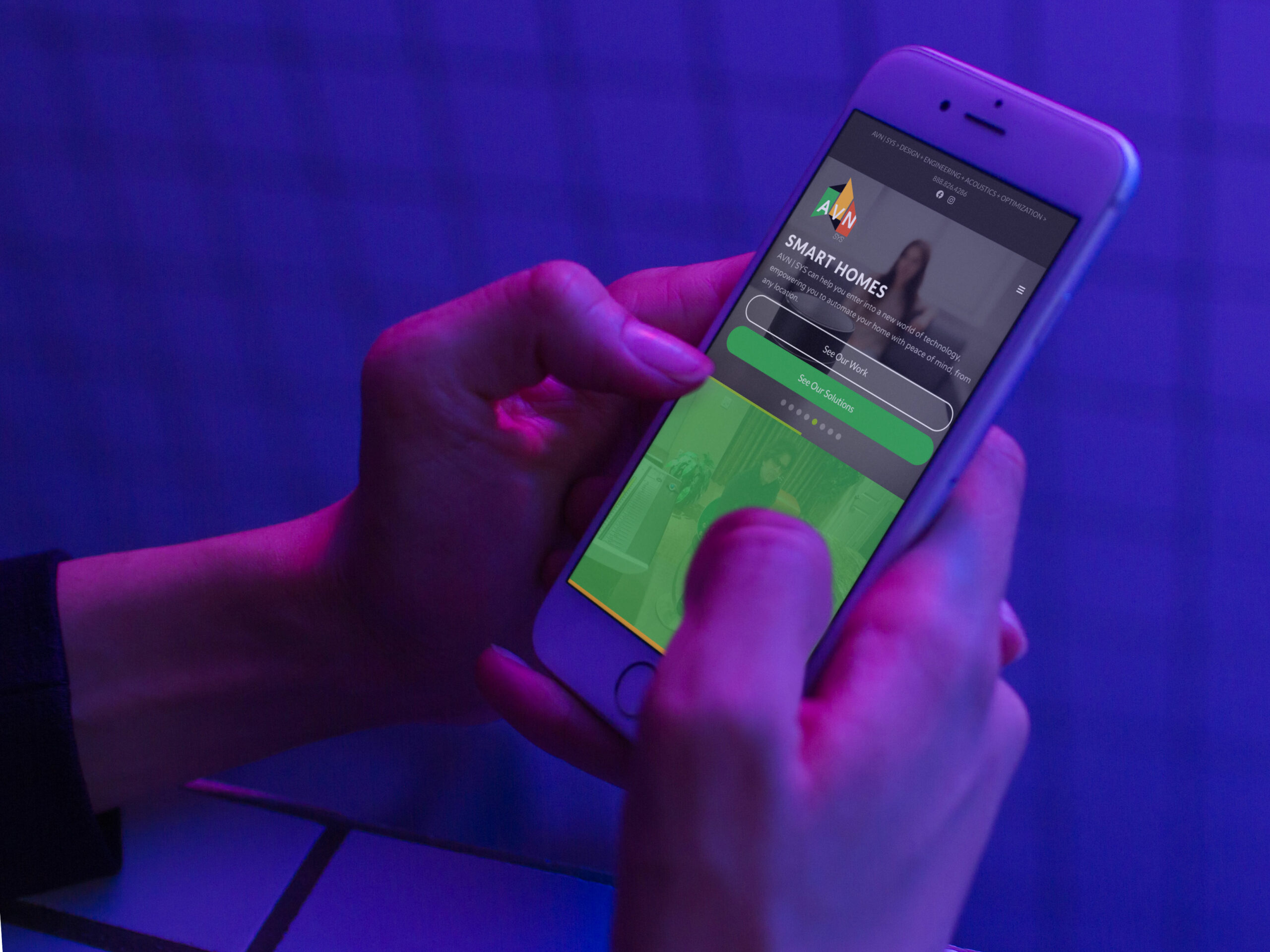 Hands hold a phone showing the Smart Homes solution page under violet light, the green AVN mark topping the mobile layout.