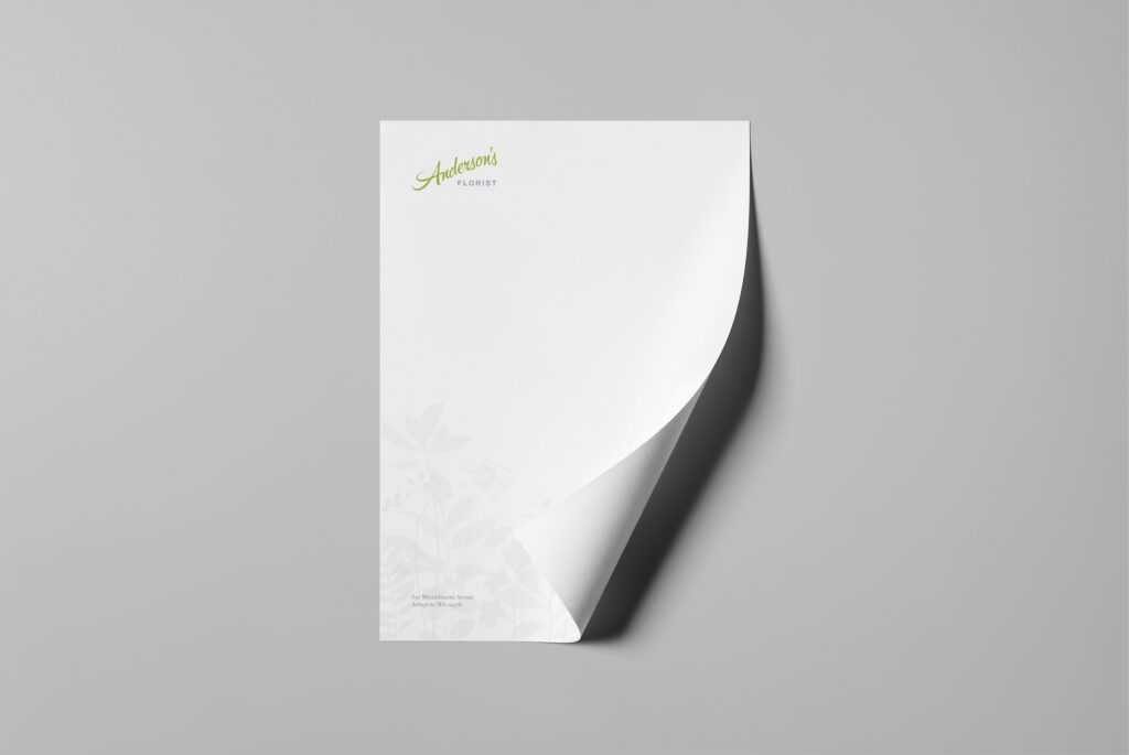 Letterhead sheet with a curled corner, the green script mark at top and ghosted floral silhouettes drifting across the lower third.