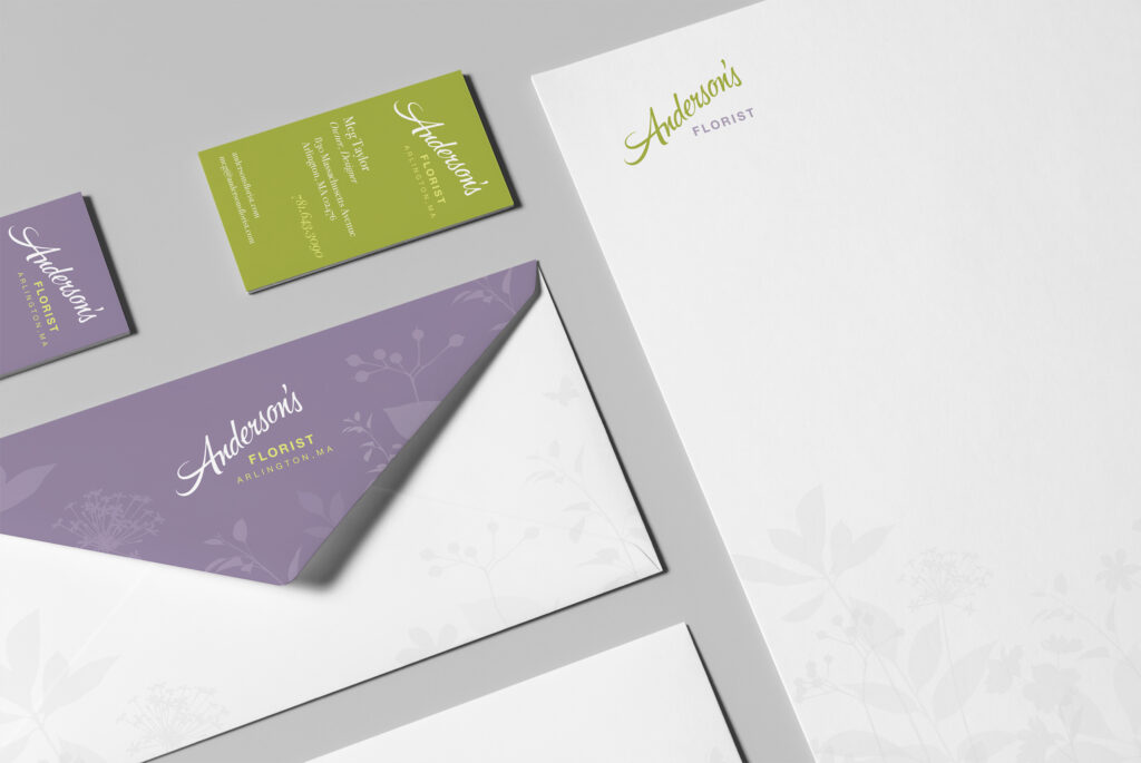 Close angle across cards, lavender envelope wrap, and letterhead, the floral silhouettes and script mark threading the set together.