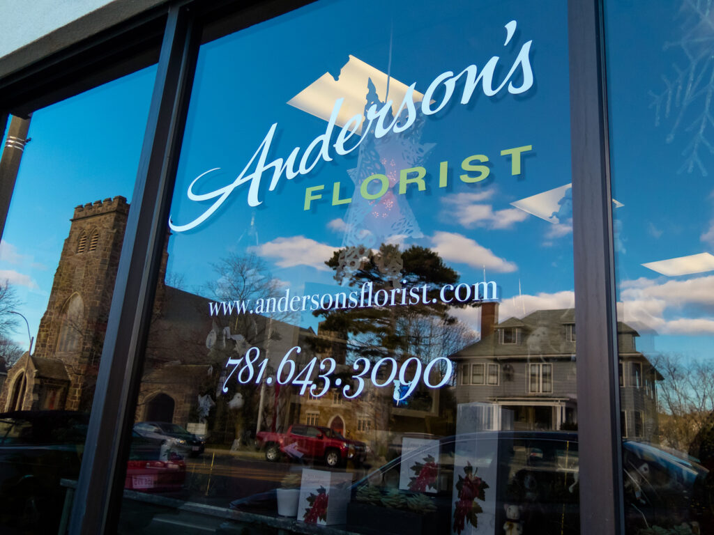 White script window lettering with the site address and phone number, a stone church and blue sky reflected across the glass.