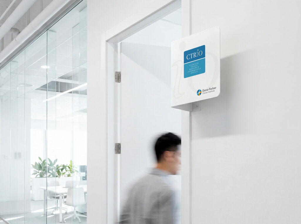 Door-mounted CTRiO blade sign paired with the Dana-Farber Cancer Institute lockup in a bright white office corridor as a staff member passes below.