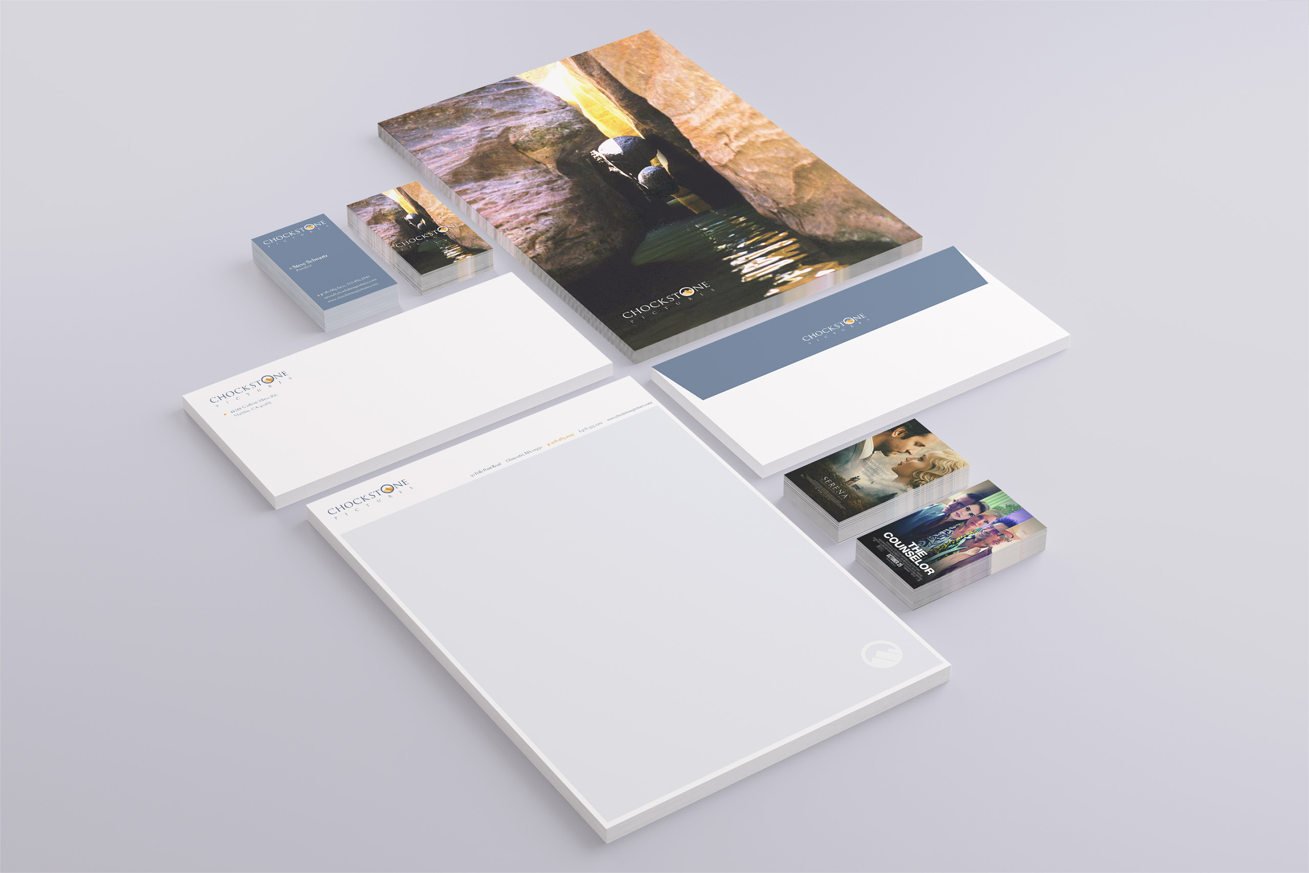 Stationery suite with canyon-photograph folder cover, slate blue envelope bands, letterhead, and film-still business cards arranged on gray.