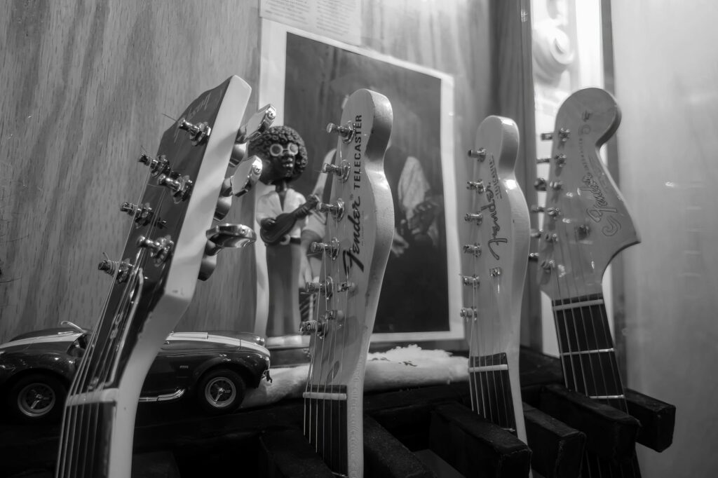 Row of guitar headstocks including a Fender Telecaster, with a figurine and a model sports car tucked among the instruments.