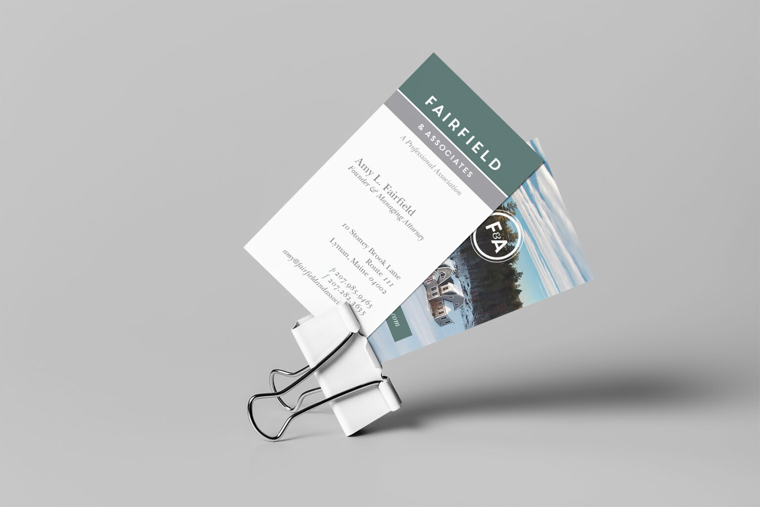 Fairfield & Associates business card held in a binder clip, Amy L. Fairfield’s card front paired with the F&A seal over a coastal photo back.