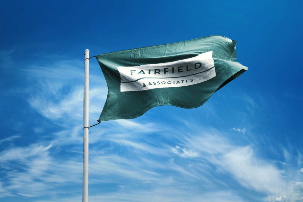 Sea-green Fairfield & Associates flag flying against a bright blue sky, the stacked wordmark bars carried on a white field.