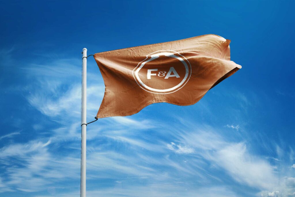 Buoy-orange flag flying against a bright blue sky, carrying the white circular F&A monogram seal at its center.