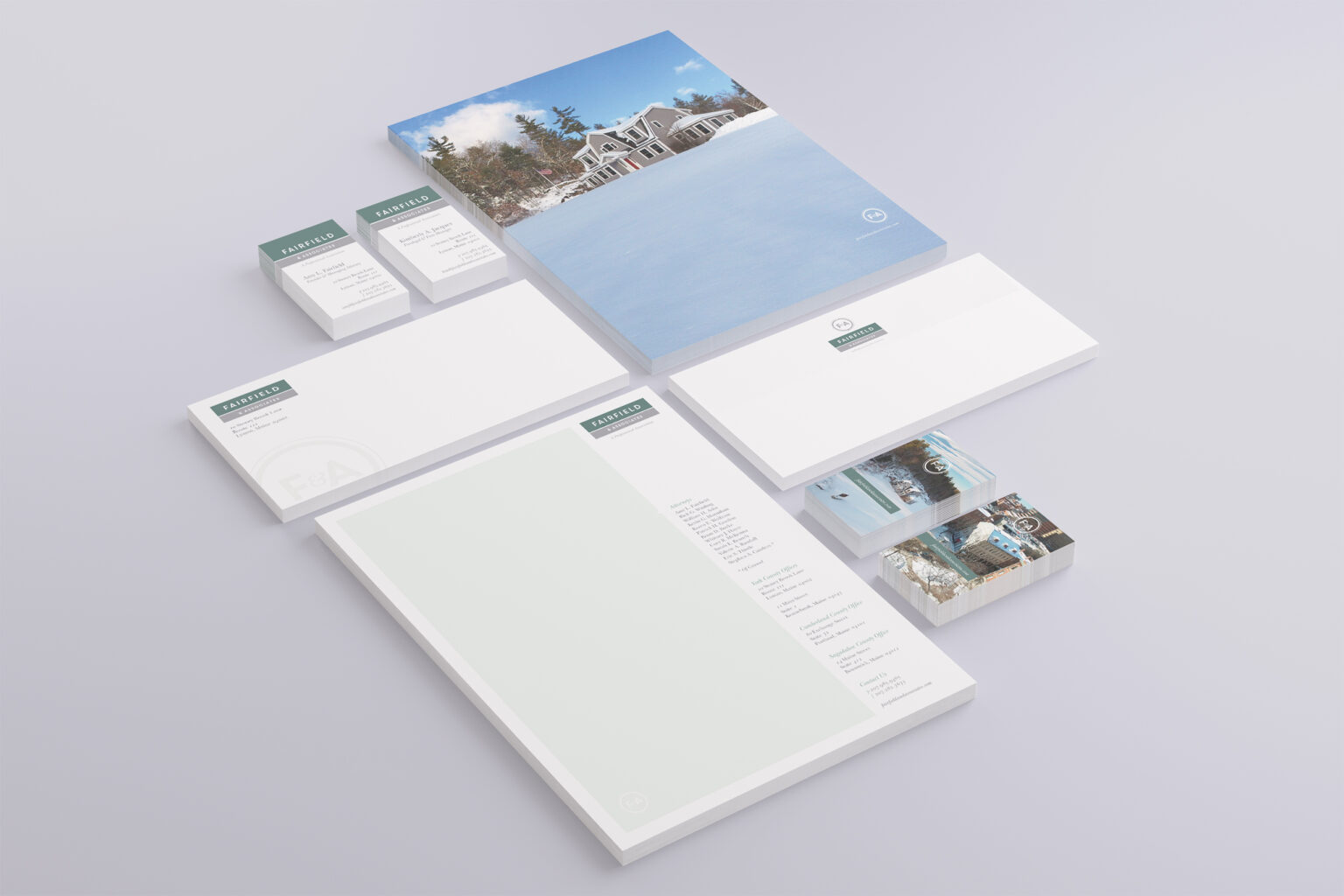 Stationery system arranged in isometric view, letterhead, envelopes, and business card stacks around a folder cover of the snowbound Lyman office.