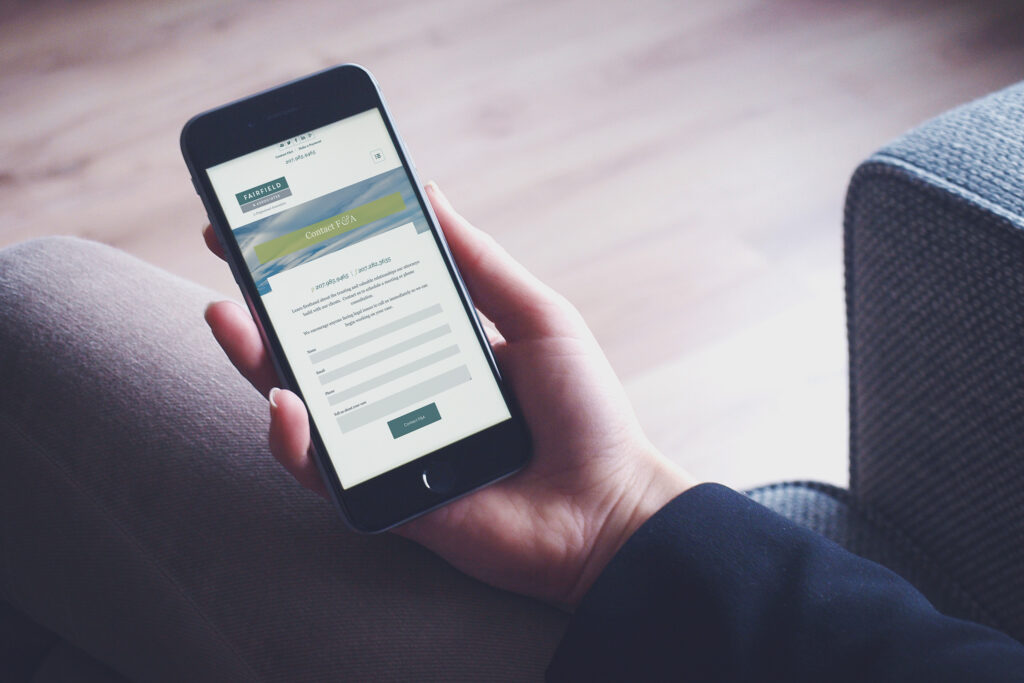 Fairfield & Associates contact page on an iPhone held in hand, the coastal-banner form ready for a consultation request from the couch.