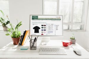 Desktop mockup of a polo shirt product detail page with color swatch selection, styled on a white desk between plants.