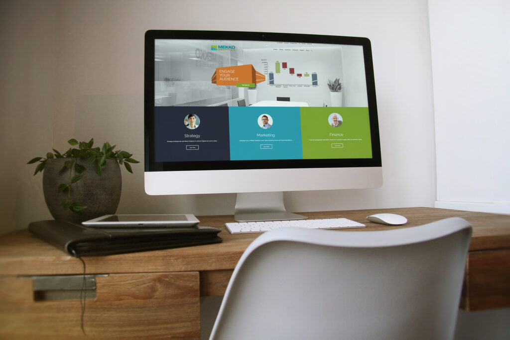 Desktop monitor on a wood desk showing the homepage hero with an orange Engage Your Audience chart over Strategy, Marketing, and Finance panels.