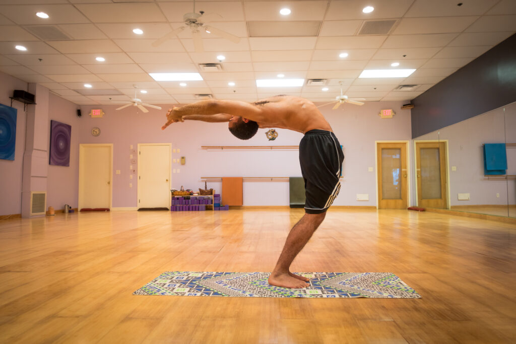 A student performing a standing backbend, known in Sanskrit as Anuvittasana, in the bright, mirror-lined Mystic Fitness studio.