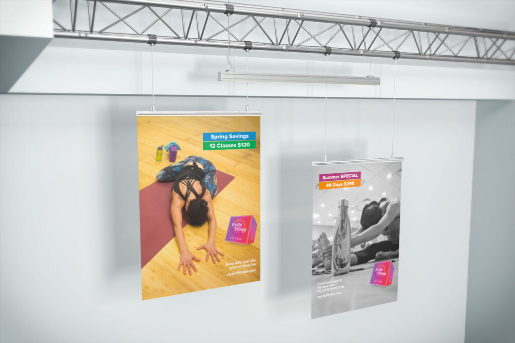 Two posters hang from a steel rail, Spring Savings 12 Classes $120 over a student in a forward fold and Summer Special 99 Days $299 over a black-and-white water bottle.