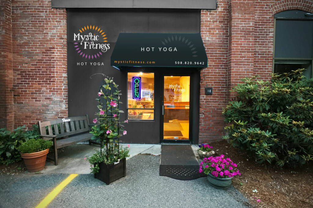 Environmental signage at the Mystic Fitness studio entrance, a brick storefront with an illuminated glass doorway framed by planters.