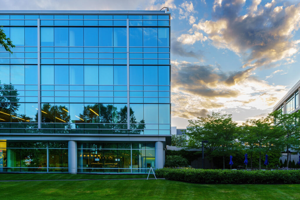 Close facade of the glass curtain wall at sunset, lit interiors showing through the ground floor beneath streaked clouds.