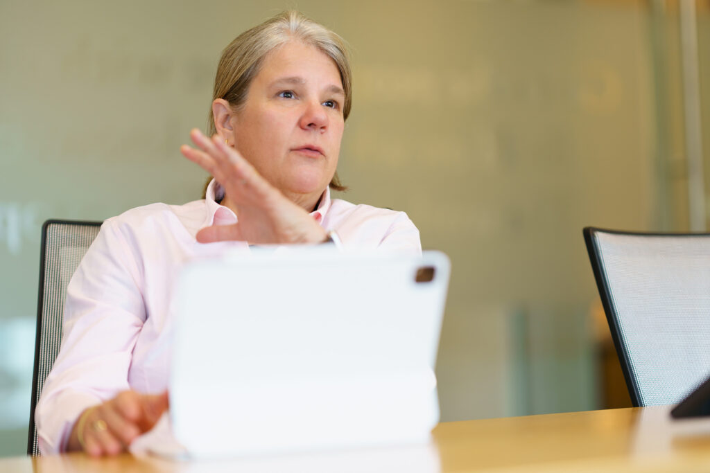 Gina Vanderloop gestures over a white tablet mid-point, seated against the etched glass wall of the meeting room.