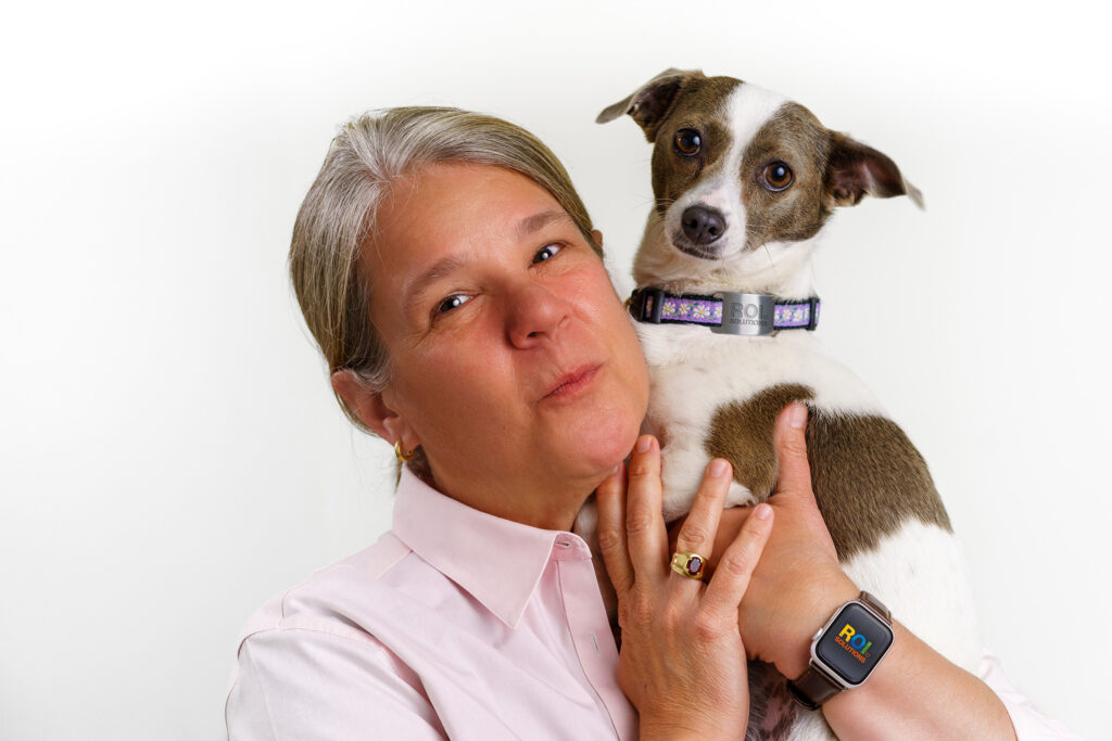 Gina Vanderloop cradles Rosie, a brown and white terrier wearing a collar, cheek to cheek against a white studio wall.