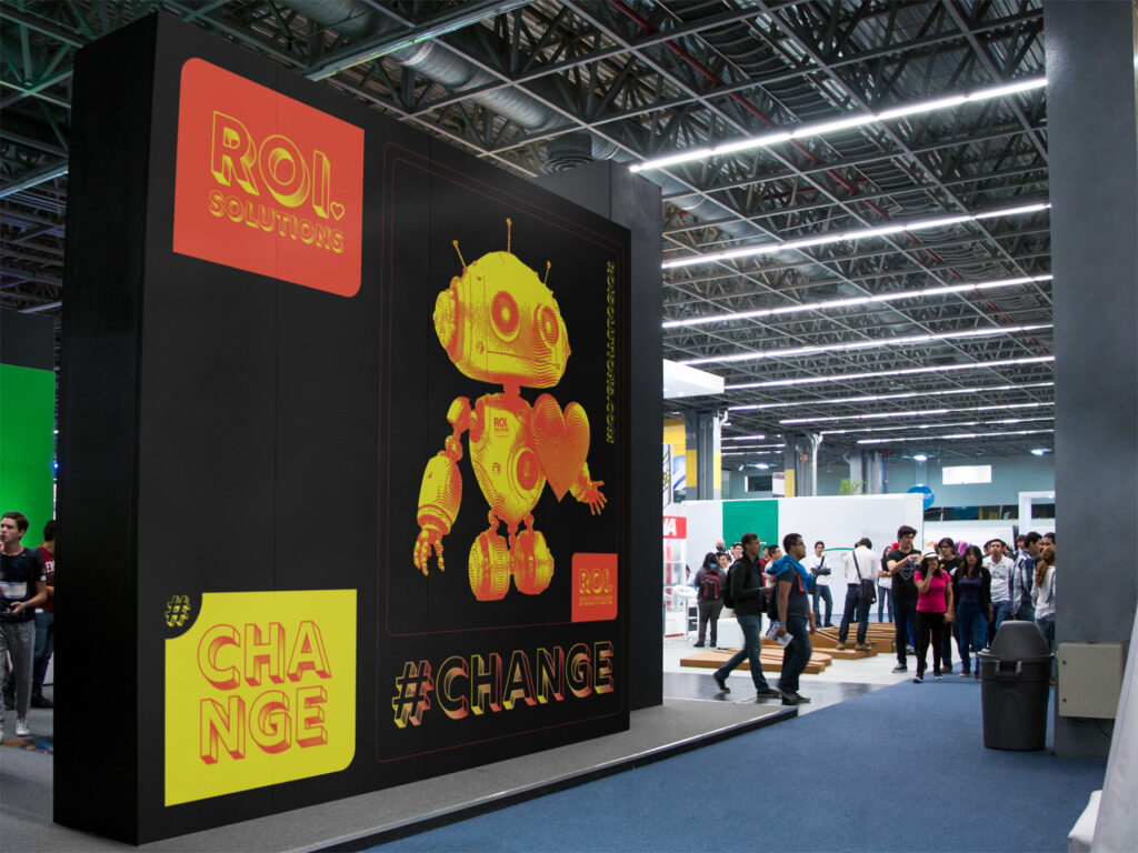 Virtual meeting backdrop of the black trade-show booth, a gold robot and hashtag Change graphics towering over the crowd.