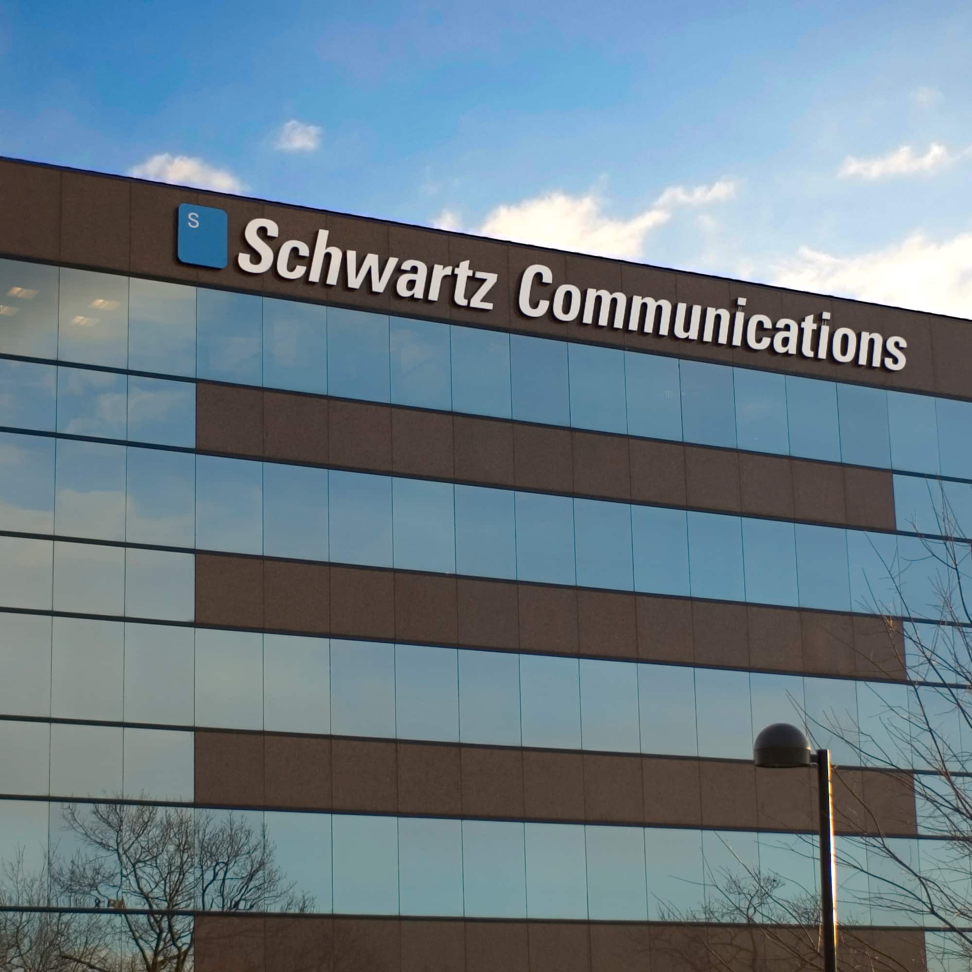 Schwartz Communications dimensional letters and the blue S badge mounted atop the glass headquarters tower against a bright sky.