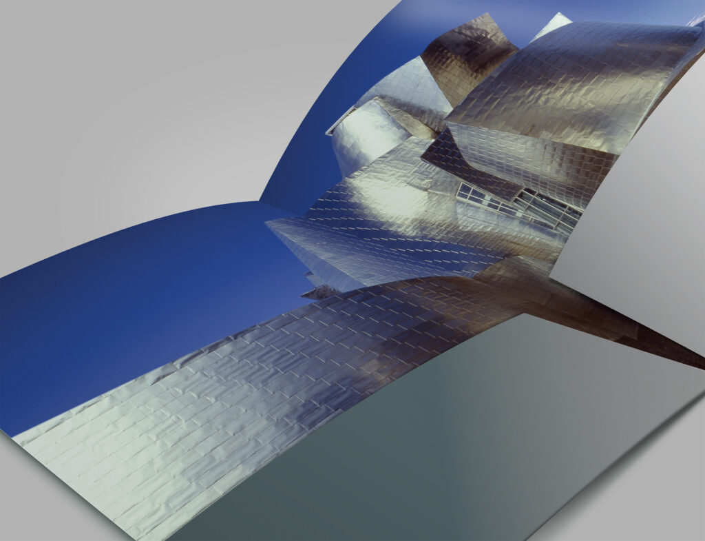 Close detail of the press kit interior, the museum’s titanium tiles and deep blue sky wrapping the folder’s gatefold.