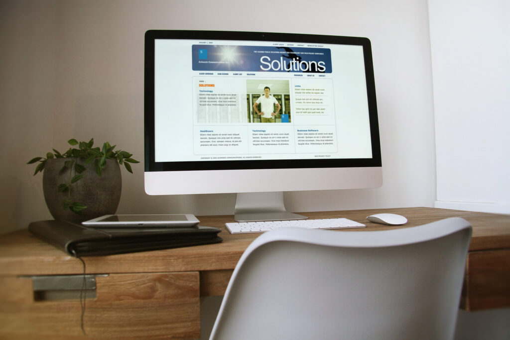 Solutions page on an iMac in a home office, technology, healthcare, and business-influencer practice columns under the blue masthead.