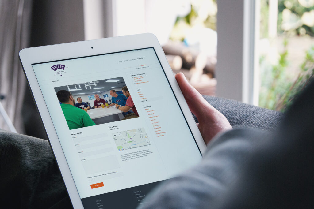 Contact page on an iPad, the team photographed mid-meeting above the mail form, map, and product directory links.