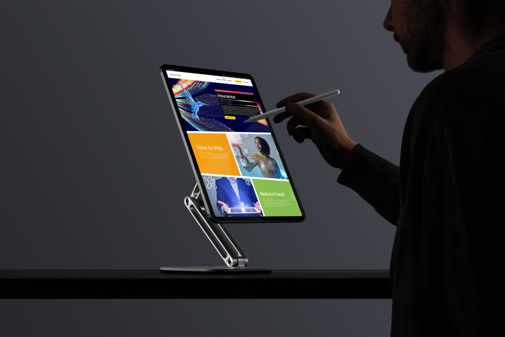 Man with a stylus works on the Insurance landing page on a stand-mounted tablet, hummingbird data art above tilted panels.