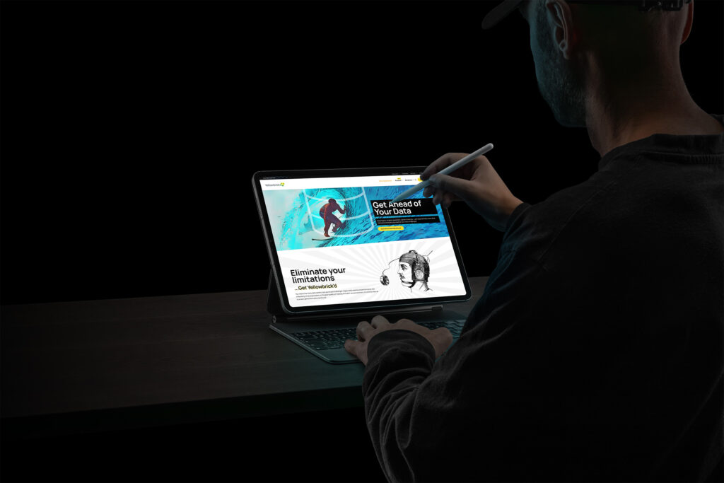Man sketches on a tablet showing the Get Ahead of Your Data page, a surfer riding a teal wave above Eliminate Your Limitations.