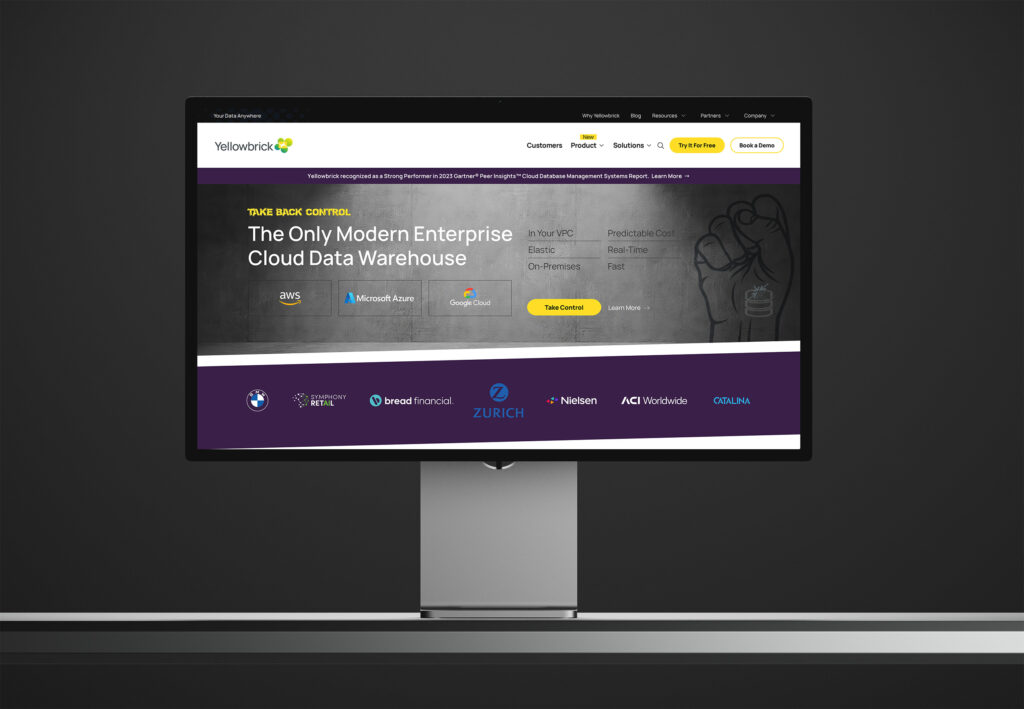 Homepage on a display in a dark room, the concrete fist hero and purple client band glowing against near-black walls.