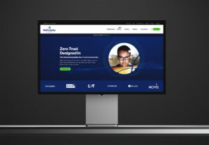 Studio display showing the Zero Trust Designed In homepage hero, a portrait in the wave ring above client logos.