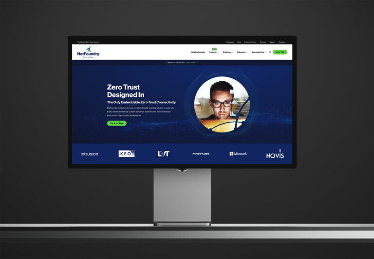 Studio display showing the Zero Trust Designed In homepage hero, a portrait in the wave ring above client logos.