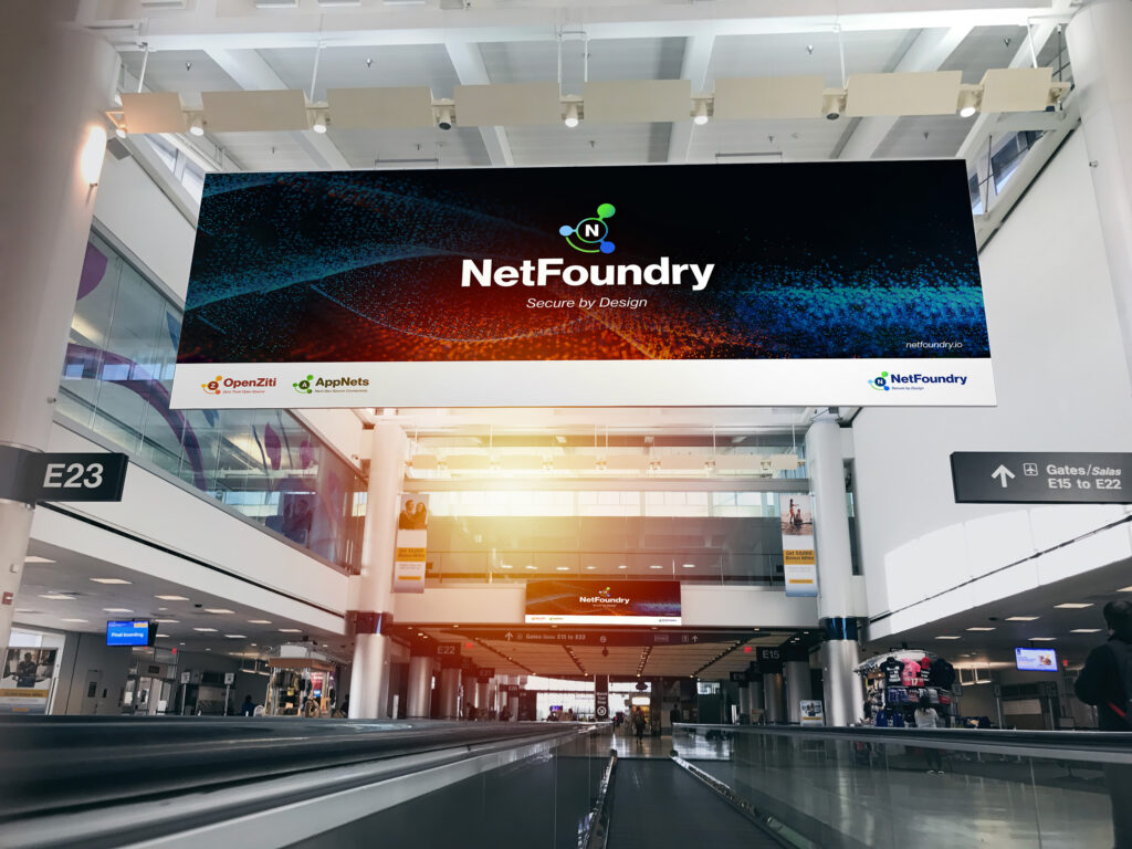 Virtual meeting backdrop of a terminal concourse, the NetFoundry billboard glowing in particle waves above the moving walkway.