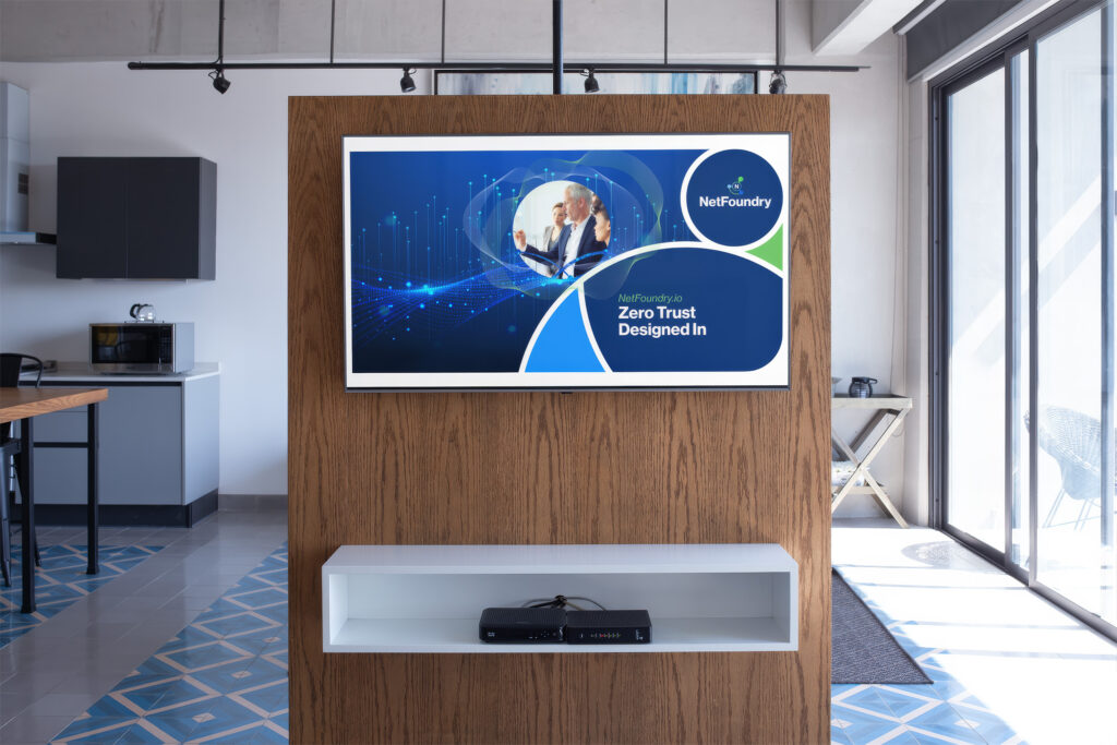Virtual meeting backdrop of an office kitchen, the Zero Trust Designed In screen mounted on a wood panel.