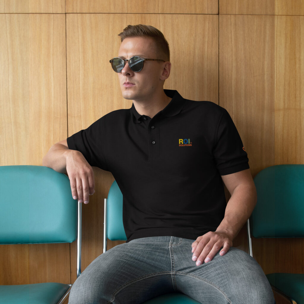 Model in sunglasses sits in the black polo, the embroidered multicolor logo on the chest.