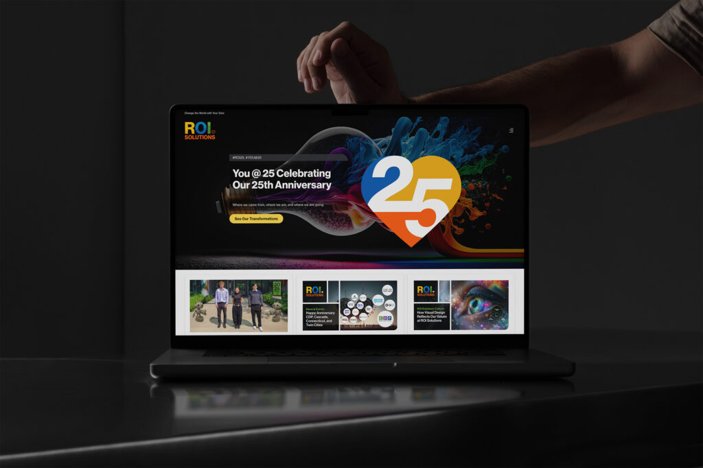 Laptop in low light showing the You at 25 anniversary page, the segmented heart bursting through paint above story cards.