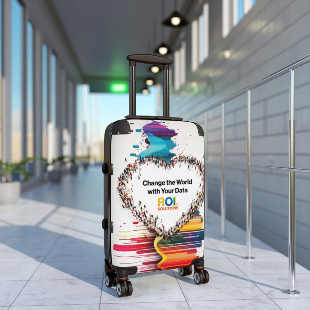 Crowd-heart carry-on spinner standing in a sunlit airport corridor, the rainbow paint streaks catching the window light.