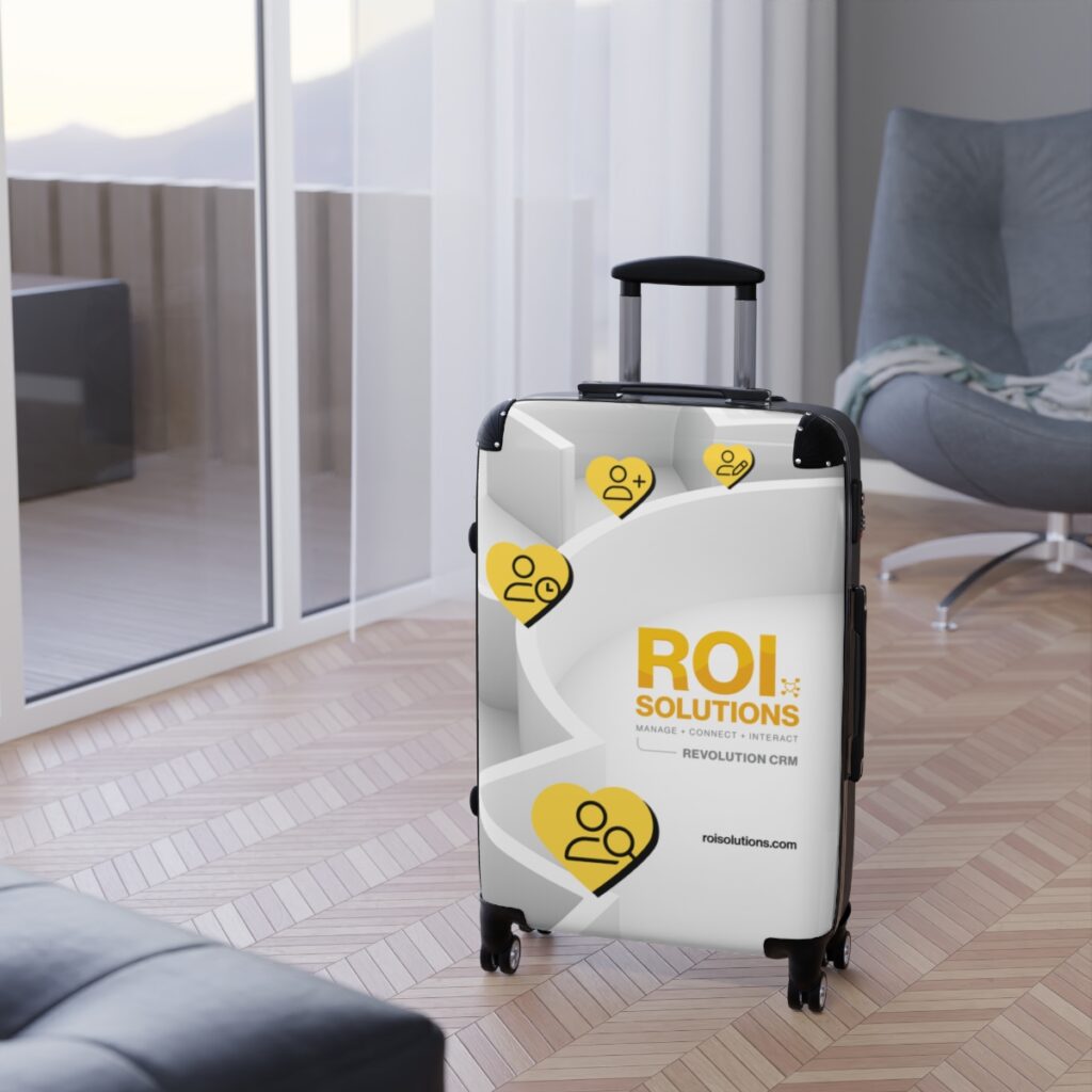 Revolution CRM carry-on spinner parked on a herringbone floor beside a gray lounge chair and glass balcony door.