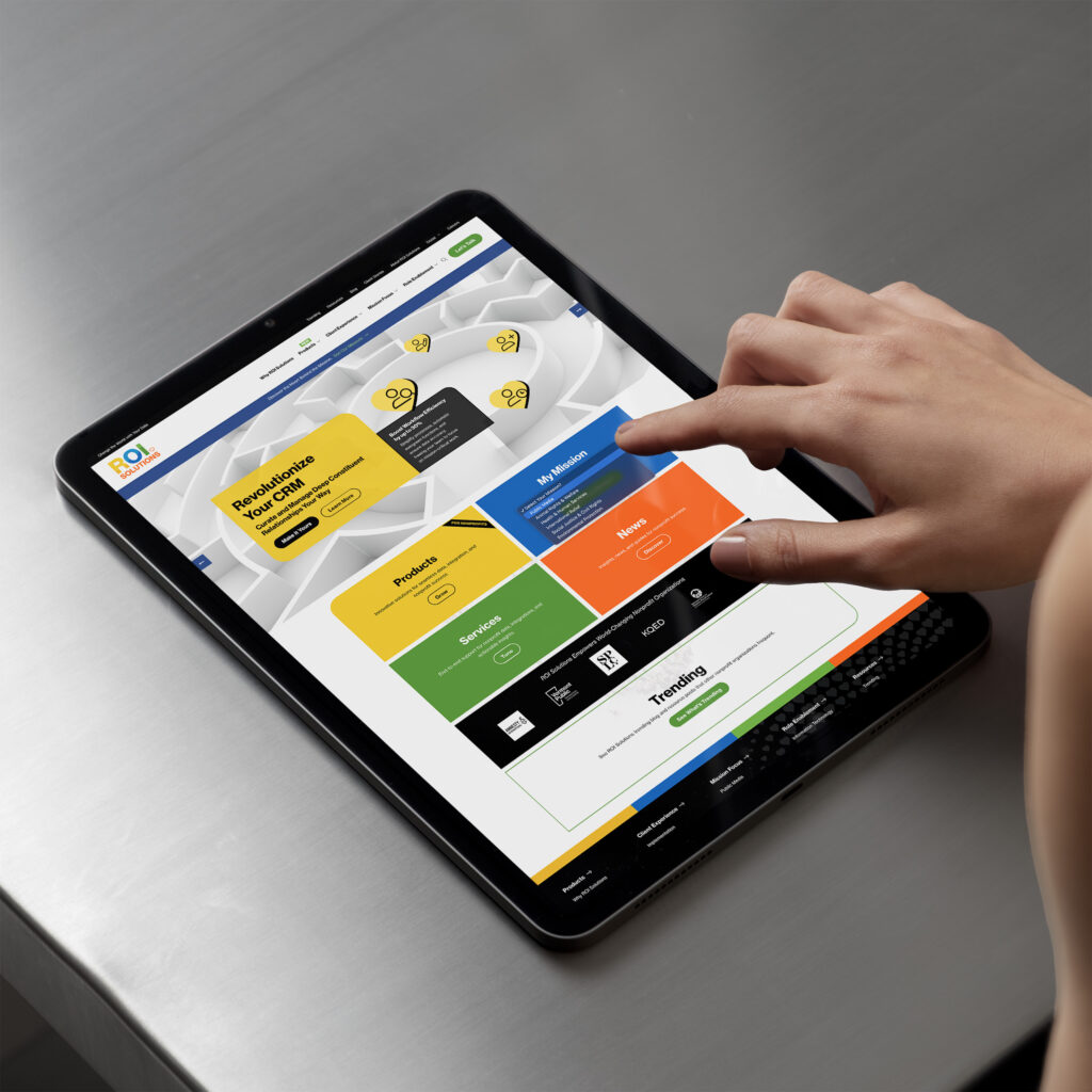 Hand taps the My Mission selector on the tablet homepage, color tiles for products, services, and news below the maze hero.