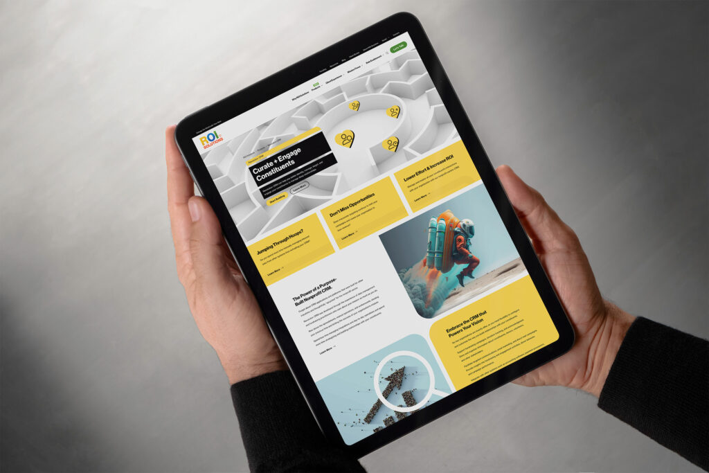 Hands hold a tablet showing the Revolution CRM page, the maze hero above yellow panels and the rocket-pack explorer.