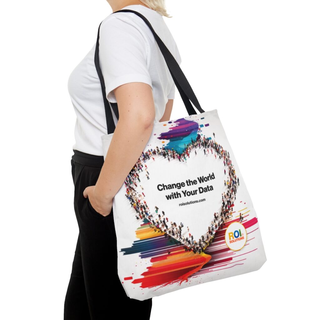 Side view of the crowd-heart tote on a shoulder, rainbow paint spilling beneath the brand promise.