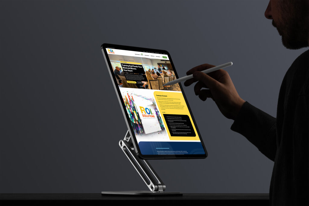 Silhouetted man with a stylus reviews the training page on a stand-mounted tablet, white-paper cards along the yellow panel.