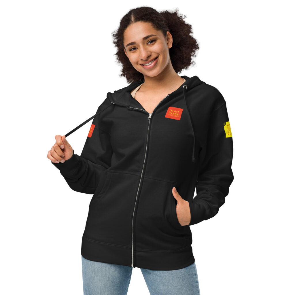 Smiling model pulls the drawstring of the black fleece zip hoodie, orange and gold product patches at chest and sleeve.