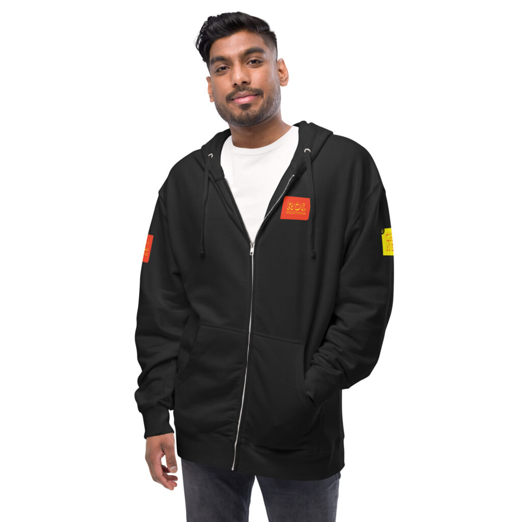 Model in a white tee wears the open black fleece hoodie, orange chest patch and gold sleeve patch showing.