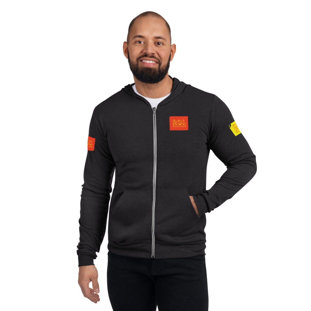 Smiling model in the charcoal triblend zip hoodie, orange chest patch and gold sleeve patch over black jeans.