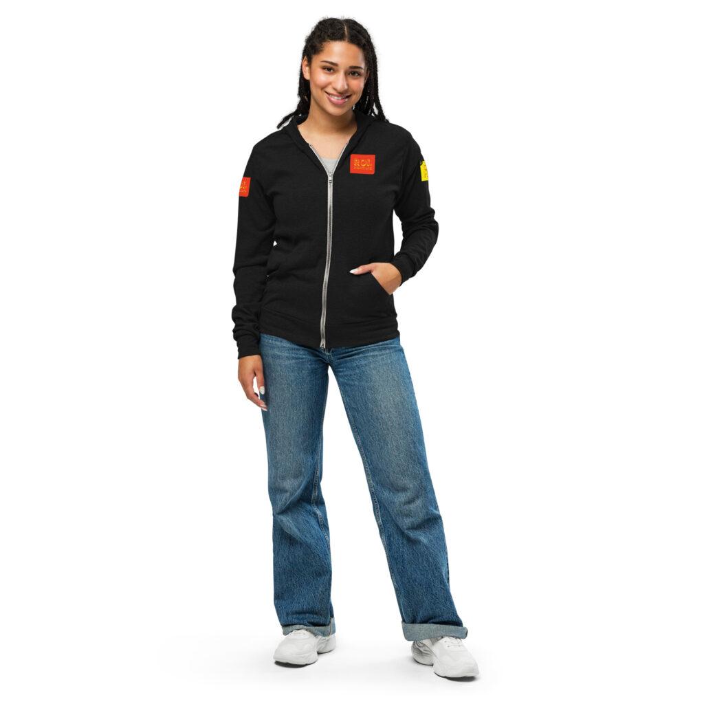 Model with hands in pockets wears the solid black triblend zip hoodie with orange and gold brand patches.