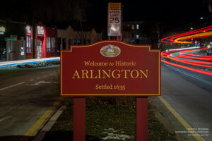 Welcome to Historic Arlington sign centered on the median at night with curving traffic light trails behind.